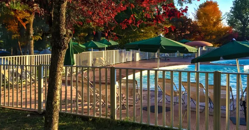 LP gas pool heater image of an outdoor, heated and fenced pool under trees showing fall leaf colors.