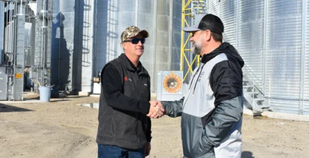 A PepUp Propane Salesman shakes hands with a local Delmarva farmer, with grain silos in the background.