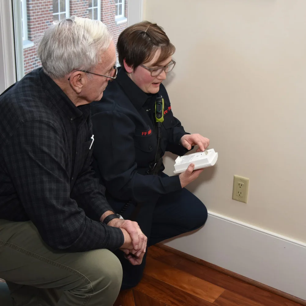 FEMA CO Detector Installation Two people install a CO and propane gas detector as directed by the manufacturer, within 1 foot of the floor, directly plugged into an outlet, with a battery backup.